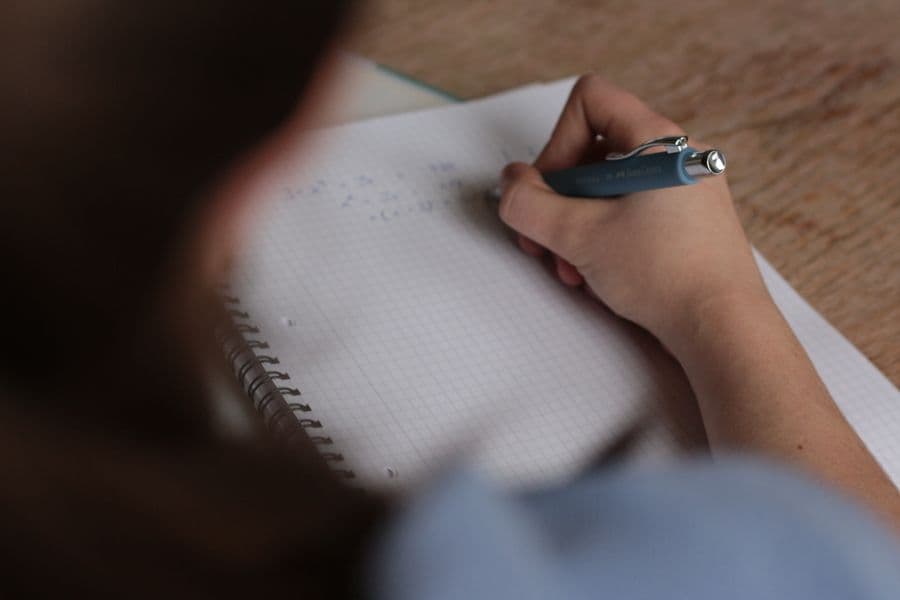 A hand writing notes beside an open book.